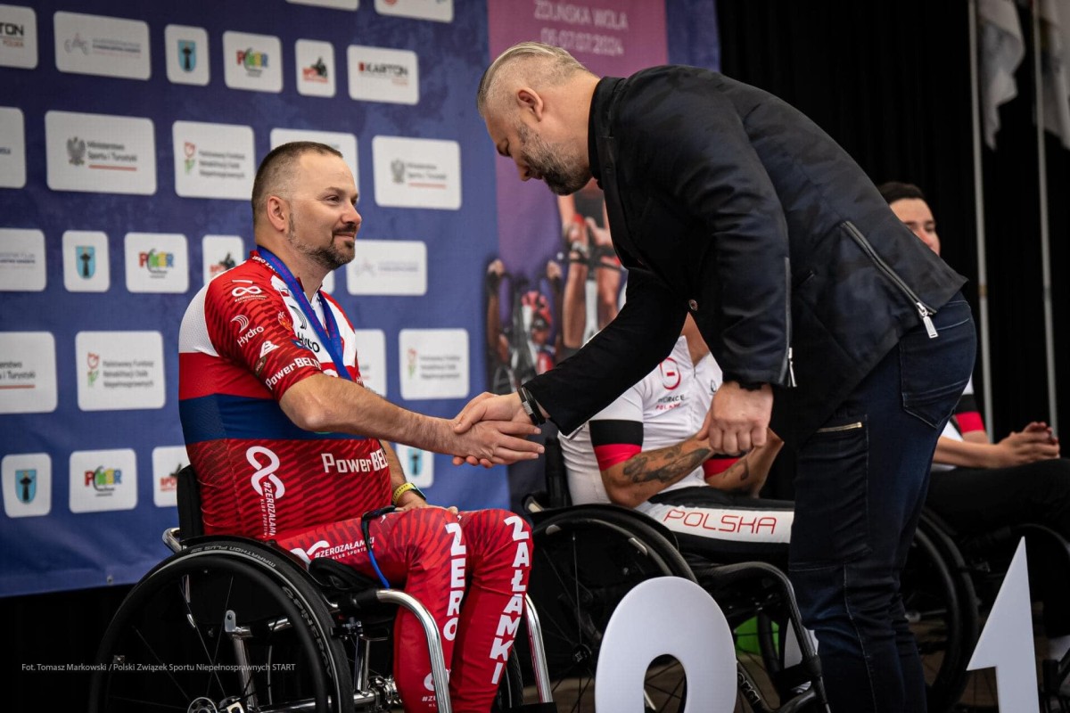 Daniel Osiński siedzący na wózku odbiera gratulacje od mężczyzny ubranego na czarno.