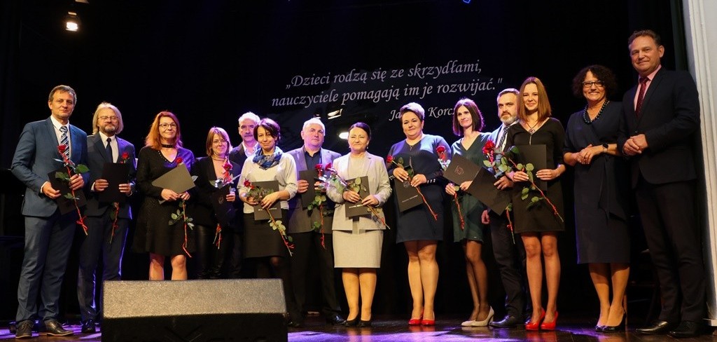 Na scenie sali widowiskowej stoją nagrodzeni nauczyciele wspólnie ze starostą i wicestarostą