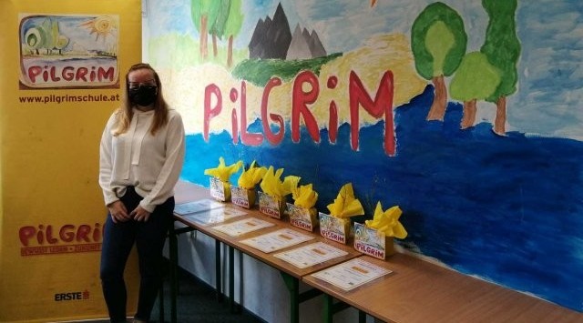 W pomieszczeniu, na tle narysowanych na ścianie elementach przyrody i napisie Pilgrim stoi kobieta ubrana w białą bluzkę i spodnie.