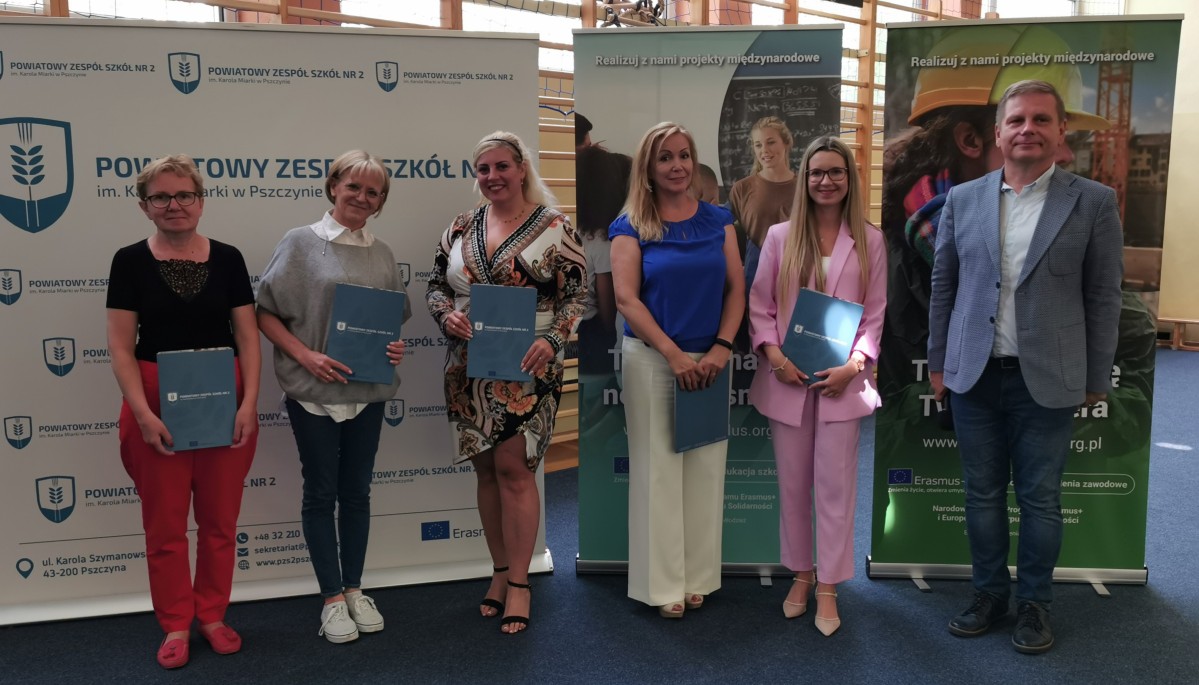 Grupa nauczycieli stoi przy bannerze szkoły wraz z dyrektorem