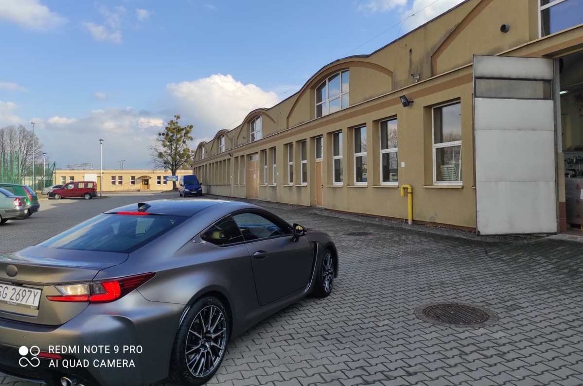 Szary samochód zaparkowany na parkingu przed warsztatami samochodowymi.