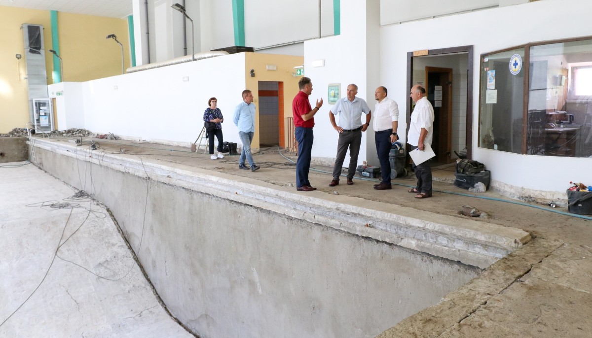Wnetrze pomieszczenia ze szkolnym basenem, po przeprowadzonych pracah rozbiórkowych. W pomieszczeniu sa włodarze powiatu, którzy oglądają stan prac.