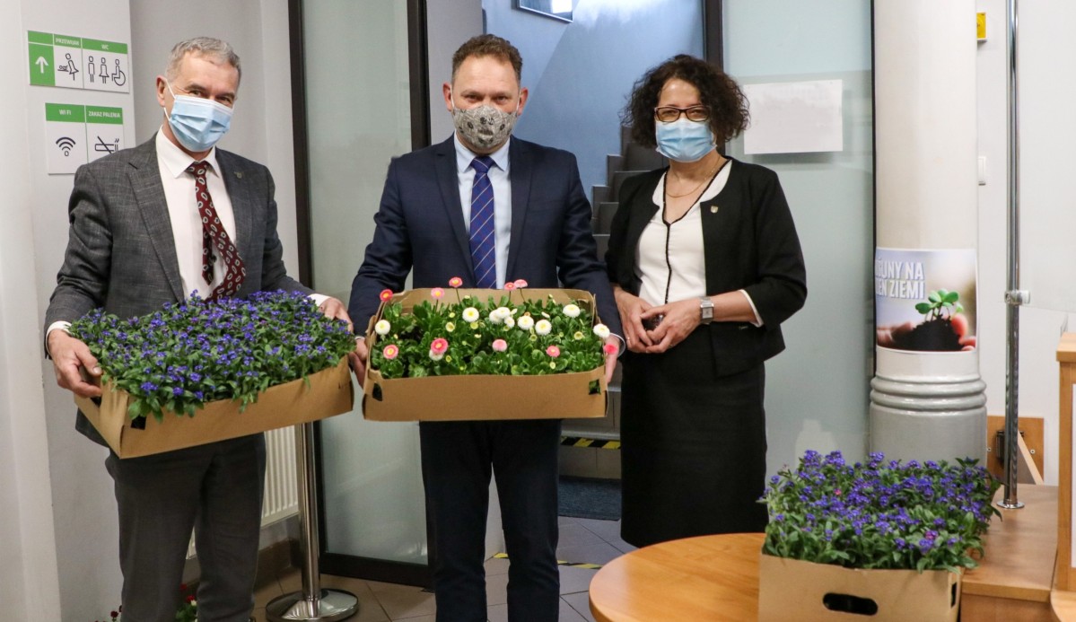 Damian Cieszewski, Grzegorz Nogły i Brabara Bandoła stoją w punkcie obsługi klienta starostwa w Pszczynie. Trzymają kwiaty, które wręczane są klientom urzędu.