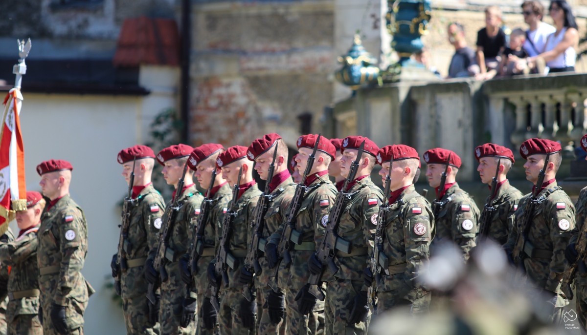 żołnierze ubrani w zielone mundury oraz czerwone berety stoja w rzędzie na dziedzińcu zamkowym