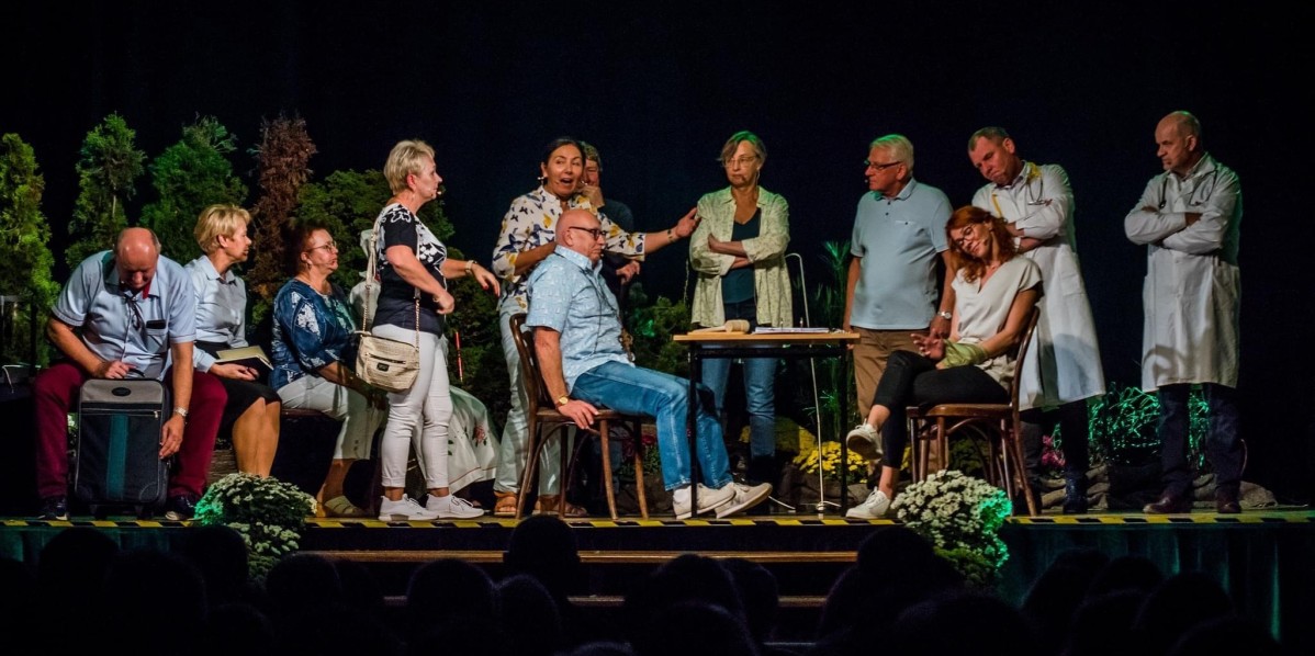 Przedstawienie teatralne w wyskonaniu amatorskiego zespołu teatralnego. Na scenie Gminnego Osrodka Kultury w Suszcu jest kilkanaście osób, część w fartuchach lekarskich