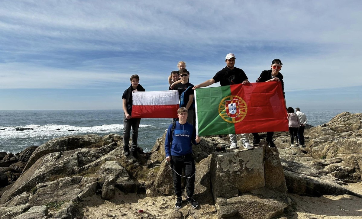 Uczniowie stoją na skałach z flagami Polski i Portugalii.