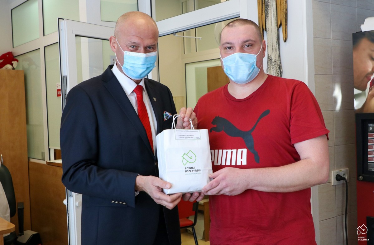 Sekretarz powiatu Szymon Sekta przekazuje białą torbę z logo powiatu ze słodyczami i gadżetami panu Tomaszowi z Tychów.