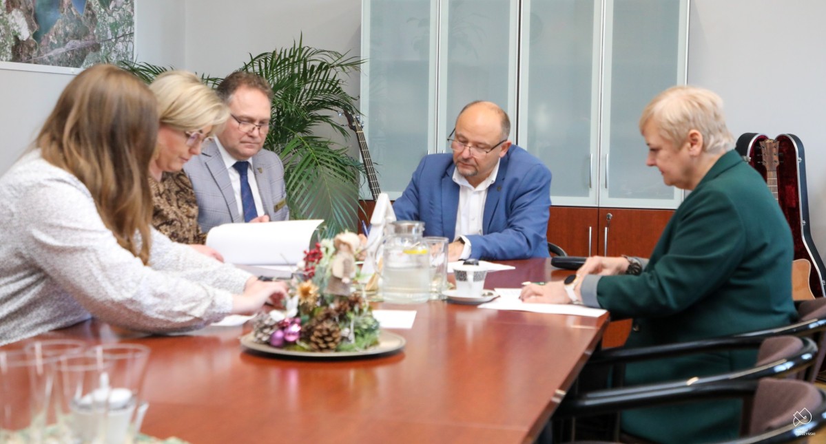 Starosta i wicestarosta podpisują umowy z przedstawicielką Dogmy. Siedzą za stołem i podpisują umowy.