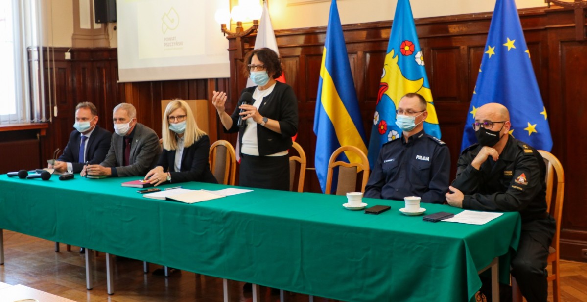 Za stołem z zielonym obrusem siedzą szefowie Powiatowego Zespołu Zarządzania Kryzysowego w Pszczynie. Przemawia starosta Barbara Bandoła
