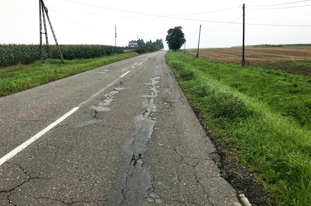 Popękana droga z licznymi ubytkami.