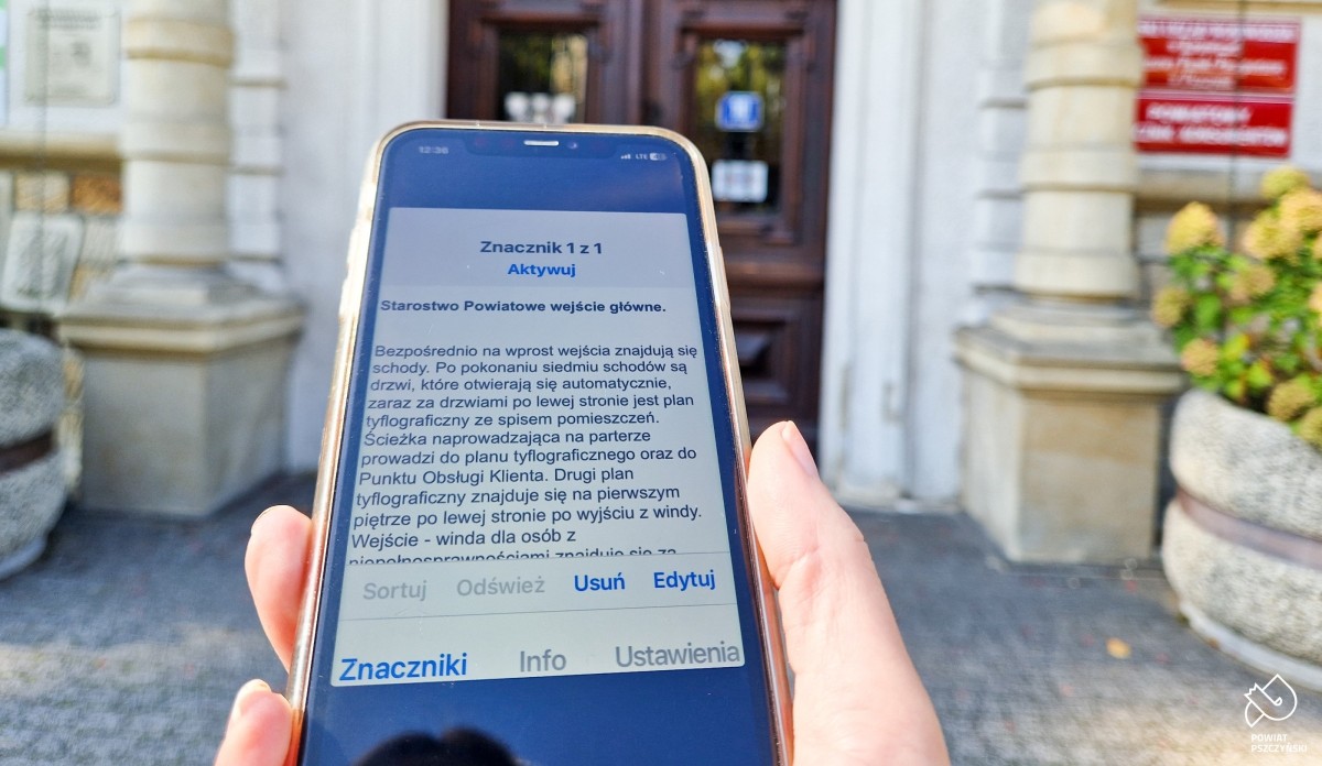 Przed budynkiem starostwa widoczny jest telefon z opisem jak wejść do budynku