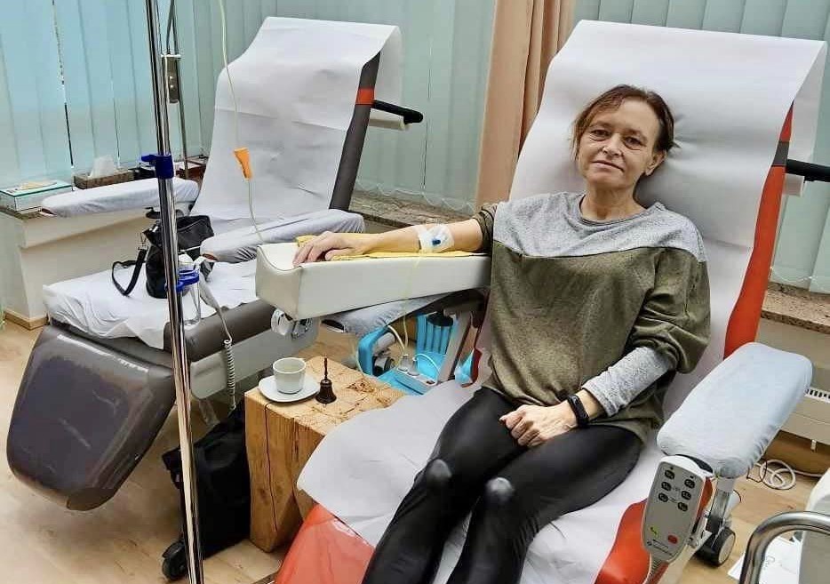 Chuda kobieta na fotelu podłączona do żółtego płynu podawanego z kroplówki.