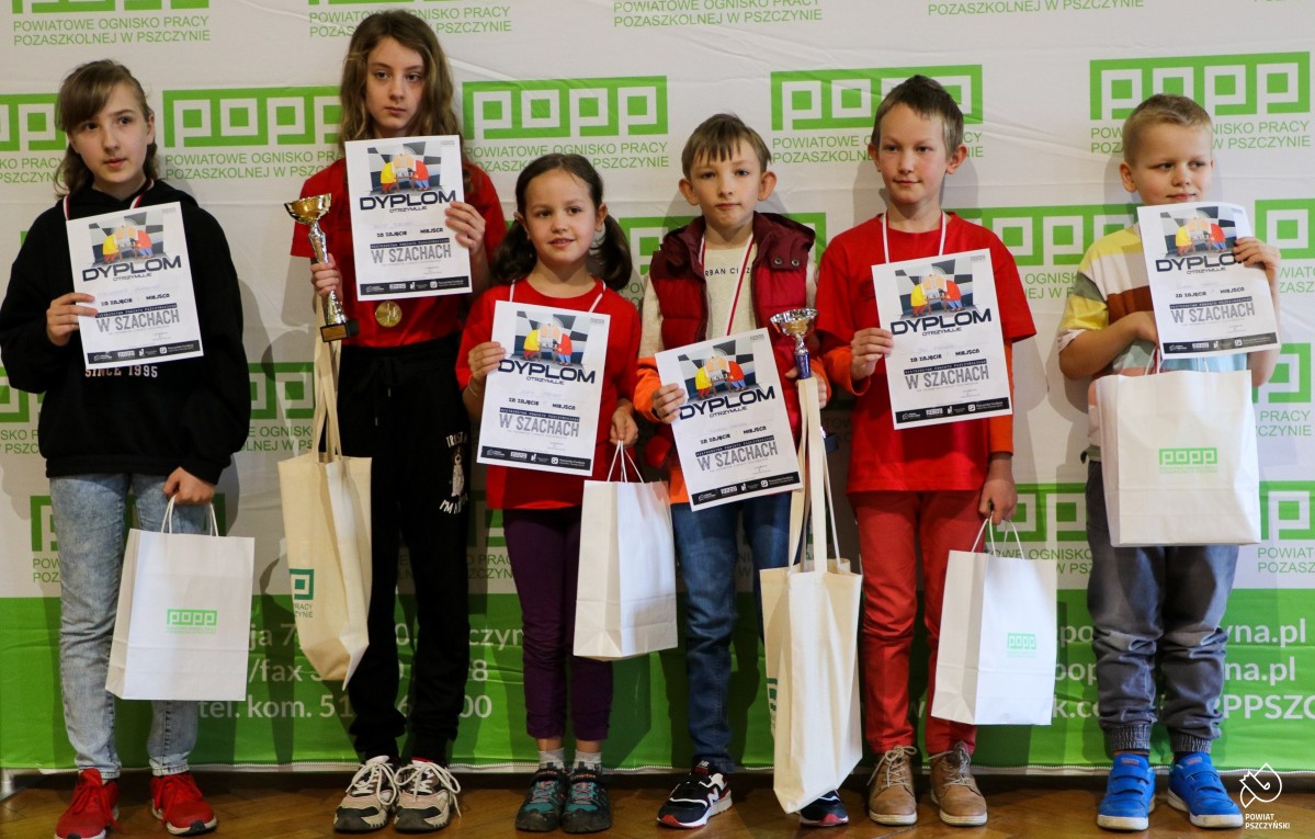 Uczniowie z dyplomami, medalami i pucharami na tle ścianki POPP.