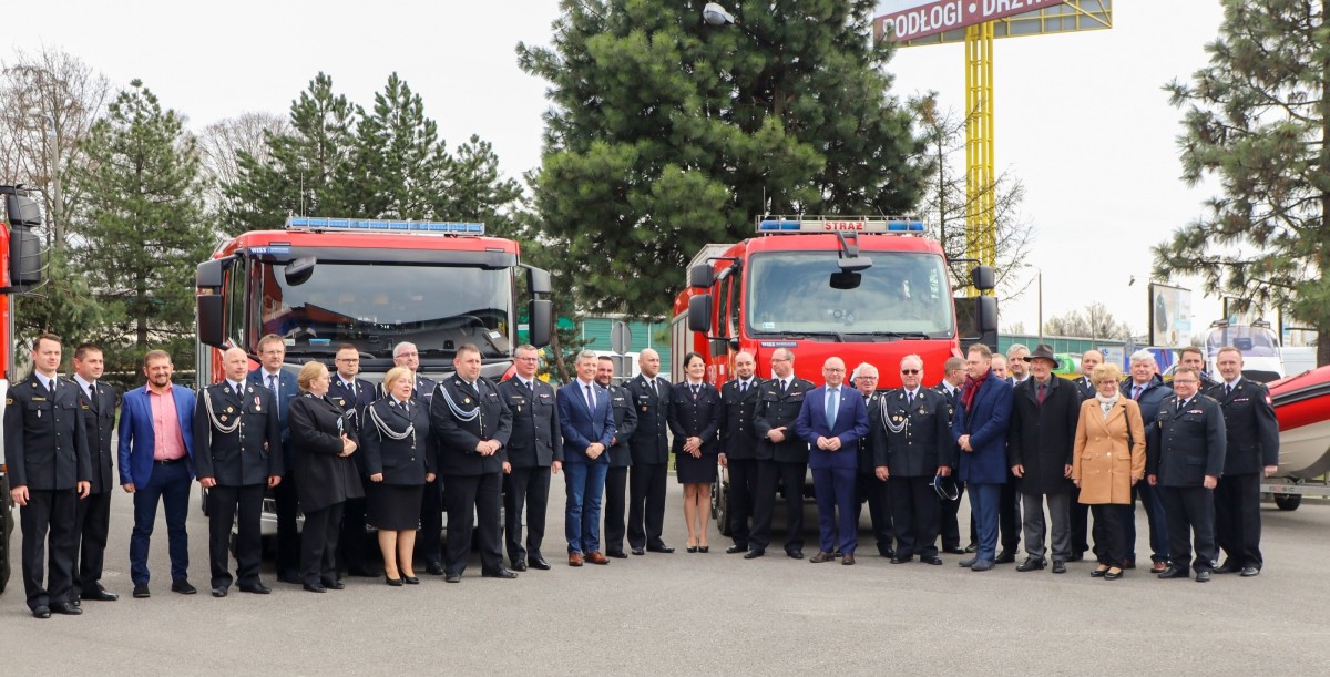 Uczestnicy spotkania na terenie komendy przed wozami strażackimi.